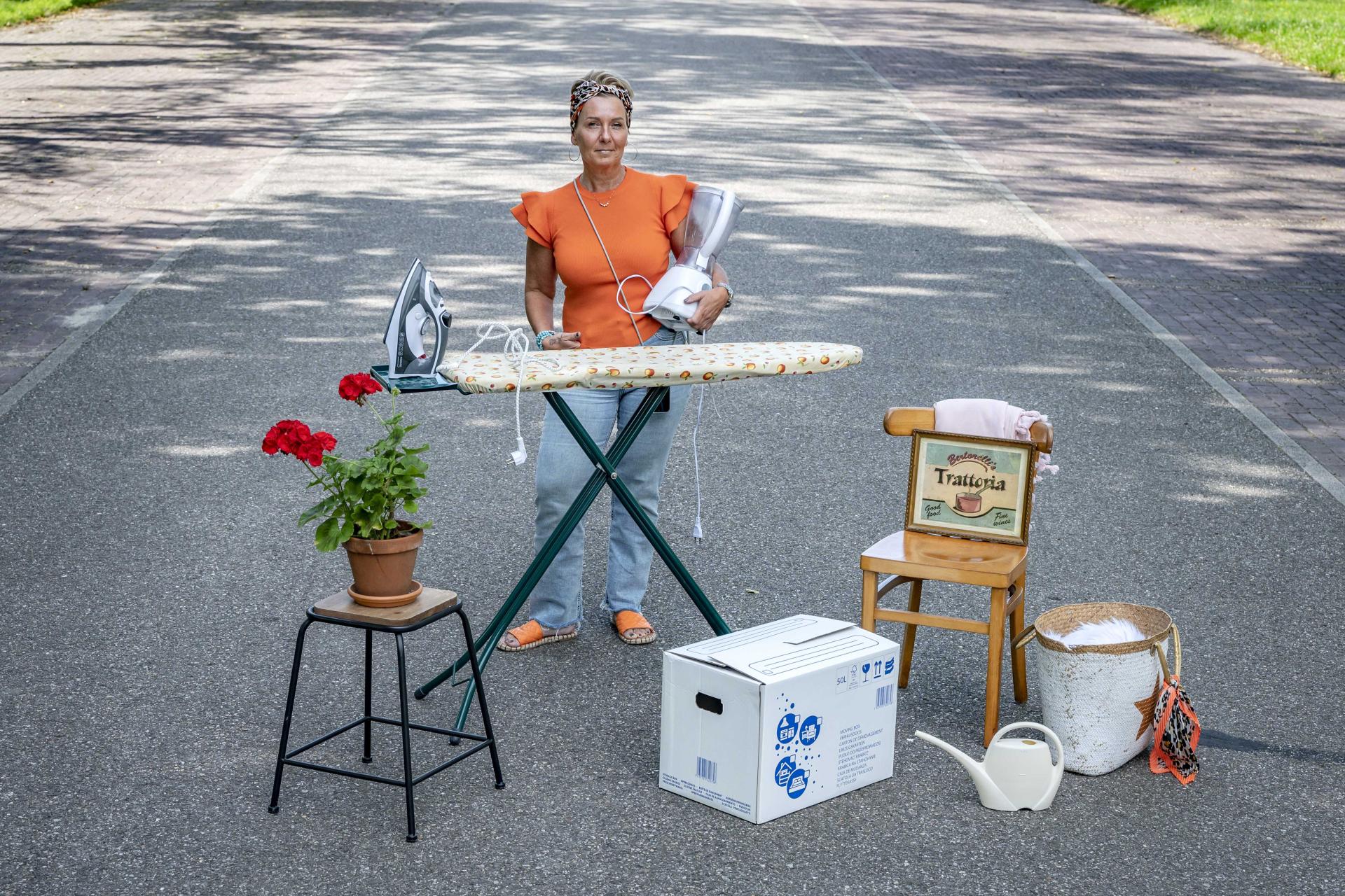 Dame die op straat staat met verhuisdozen, een strijkplank en een plant